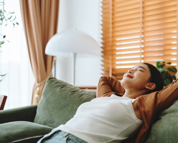 Relaxed young Asian woman enjoying rest on comfortable sofa, calm attractive girl relaxing on couch, breathing fresh air with eyes closed, meditating at home